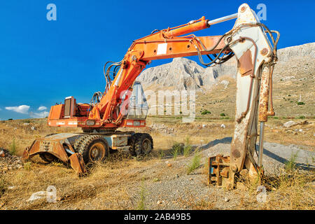 Vista laterale del braccio lungo del escavatore in una miniera con sabbia, terra e ghiaia intorno per lavori di costruzione in un suggestivo sito in costruzione. Lavori in corso Foto Stock