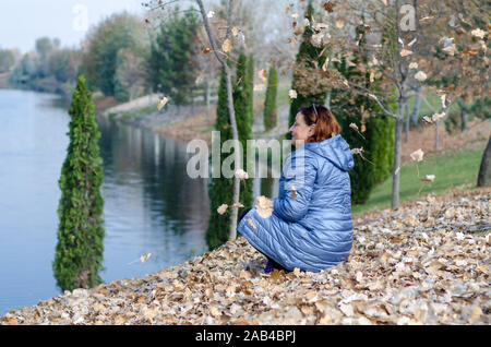 La donna di mezza età è giocare con le foglie di autunno in autunno Foto Stock