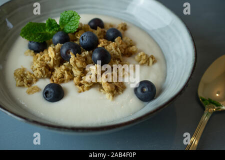 Fotografia di cibo di colazione consistente di yogurt, muesli e cereali mirtilli su uno sfondo blu Foto Stock