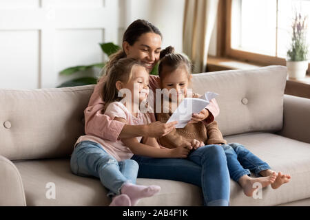 Felice giovane madre libro lettura abbracciare figlioli figlie Foto Stock