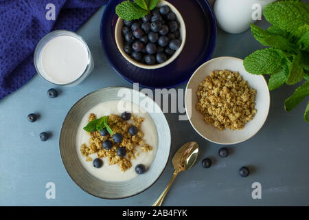 Fotografia di cibo di colazione consistente di yogurt, muesli e cereali mirtilli su uno sfondo blu Foto Stock