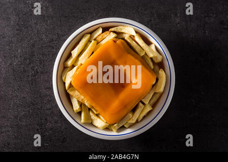 Tipica portoghese francesinha panino con patatine fritte su sfondo nero. Vista dall'alto. Foto Stock