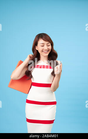 Piuttosto sorridente donna asiatica con le borse della spesa che mostra la carta di credito in mano studio shot isolato su sfondo blu Foto Stock