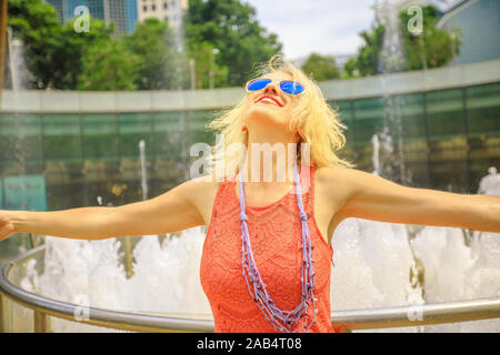 Blonde tourist godendo presso la Fontana della Ricchezza a Suntec Tower la più grande fontana in Singapore. Lo stile di vita della donna a piedi e toccare l'acqua della fontana Foto Stock