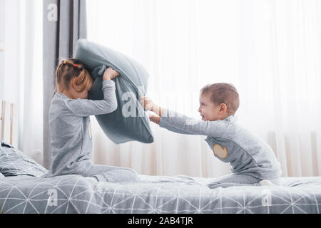 Piccolo Ragazzo e ragazza in scena una lotta di cuscini sul letto in camera da letto. Bambini cattivi battere ogni altri cuscini. A loro piace quel tipo di gioco Foto Stock