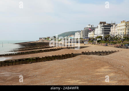 Hotel sul lungomare e pennelli multipli sulla spiaggia di Eastbourne, visto qui su un nuvoloso giorno nel maggio 2019. Foto Stock