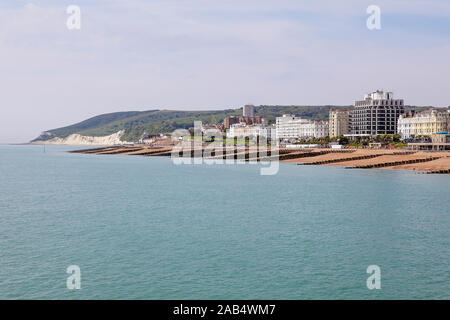 Hotel sul lungomare e pennelli multipli sulla spiaggia di Eastbourne, visto qui su un nuvoloso giorno nel maggio 2019. Foto Stock