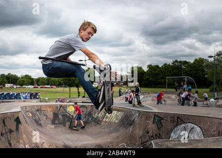 Uno dei migliori del Regno Unito scooteristi Josh praticanti di vetro presso il locale skatepark, fare acrobazie in tutto il skatepark con persone che guardano sul Foto Stock