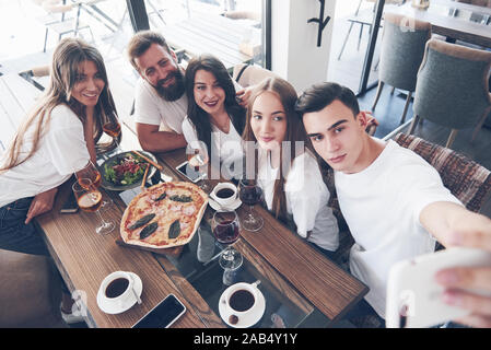 Un gruppo di persone che fanno un selfie foto in una caffetteria. I migliori amici radunati insieme a un tavolo per la cena di mangiare la pizza e il canto bevande varie Foto Stock