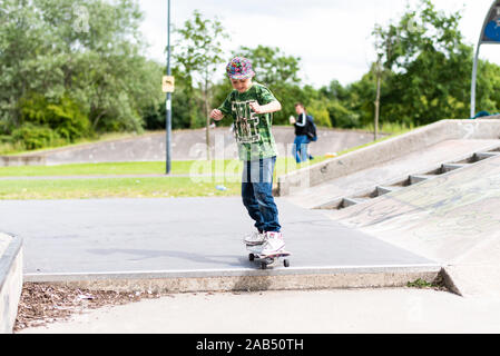 Un ragazzino con ADHD, autismo, sindrome di Asperger pratica scendendo alcuni scalini presso il locale skatepark con il suo istruttore di skateboard guardando su Foto Stock