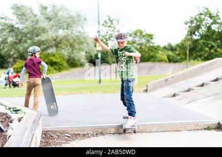 Un ragazzino con ADHD, autismo, sindrome di Asperger pratica scendendo alcuni scalini presso il locale skatepark con il suo istruttore di skateboard guardando su Foto Stock