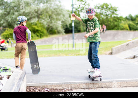 Un ragazzino con ADHD, autismo, sindrome di Asperger pratica scendendo alcuni scalini presso il locale skatepark con il suo istruttore di skateboard guardando su Foto Stock