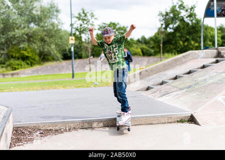 Un ragazzino con ADHD, autismo, sindrome di Asperger pratica scendendo alcuni scalini presso il locale skatepark con il suo istruttore di skateboard guardando su Foto Stock