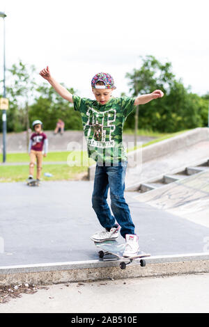 Un ragazzino con ADHD, autismo, sindrome di Asperger pratica scendendo alcuni scalini presso il locale skatepark con il suo istruttore di skateboard guardando su Foto Stock