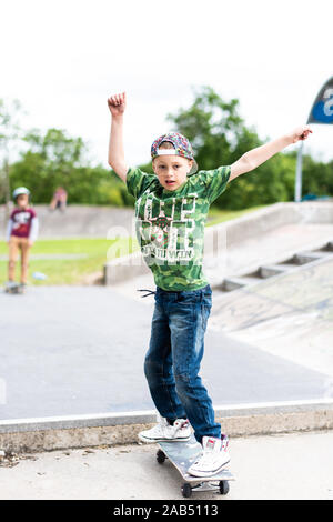 Un ragazzino con ADHD, autismo, sindrome di Asperger pratica scendendo alcuni scalini presso il locale skatepark con il suo istruttore di skateboard guardando su Foto Stock