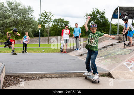 Un ragazzino con ADHD, autismo, sindrome di Asperger pratica scendendo alcuni scalini presso il locale skatepark con il suo istruttore di skateboard guardando su Foto Stock