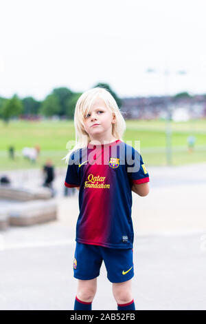 Una graziosa bambina indossa la sua preferita Barcellona kit calcio mentre fuori all'skatepark, parco in posa e guardando pensieroso Foto Stock
