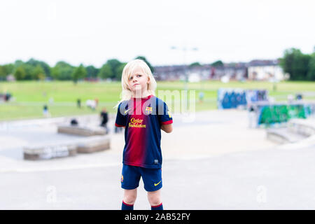 Una graziosa bambina indossa la sua preferita Barcellona kit calcio mentre fuori all'skatepark, parco in posa e guardando pensieroso Foto Stock