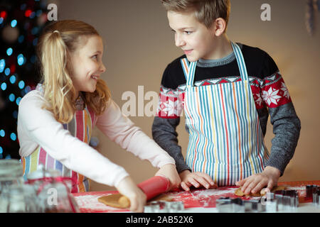 Felice teen fratelli figli la preparazione di biscotti di Natale a casa con albero di natale sullo sfondo Foto Stock