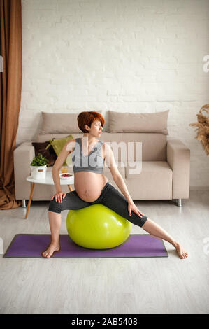 Ritratto di una giovane e bella donna incinta. Esercizi con fitball a casa. Lavoro fuori, yoga e fitness, il concetto di gravidanza. Foto Stock