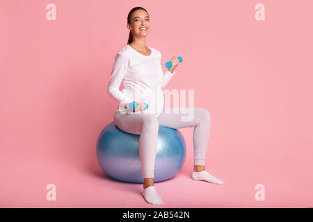 Gestanti Lady Esercizio con manubri seduti su Fitball, Studio Shot Foto Stock