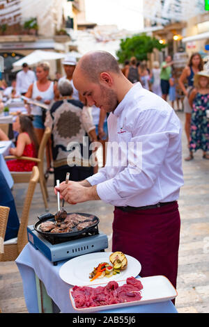 ALCUDIA, Spagna - Luglio 8, 2019: Ristorante tavoli su strada con i turisti in mare Alcudia città vecchia, isola di Mallorca, Spagna Foto Stock