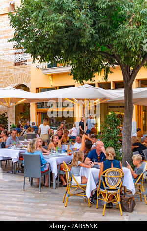 ALCUDIA, Spagna - Luglio 8, 2019: Ristorante tavoli su strada con i turisti in mare Alcudia città vecchia, isola di Mallorca, Spagna Foto Stock