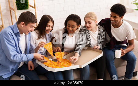 Teen coinquilini di mangiare pizza calda, prendendo fette dalla casella di consegna Foto Stock