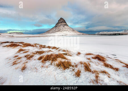 Famosa montagna con cascate in Islanda, kirkjufell, inverno in Islanda, ghiaccio e neve, riflessioni, giallo Erba, natura, ic Foto Stock