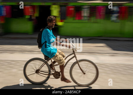 Un locale Belizean uomo in sella alla sua moto a piedi nudi per la strada di Ambergris Caye indossando un turchese brillante tee-shirt. Vi è un verde chiaro usato clo Foto Stock