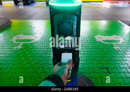 Un uomo paga per la ricarica di un auto elettrica. Mano azienda catd a pagare alla stazione di carica. Concetto di elettricità verde, ambiente pulito, emissione Foto Stock