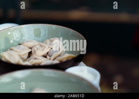 Canederli di carne russo pelmeni con pepe e panna acida nel recipiente Foto Stock