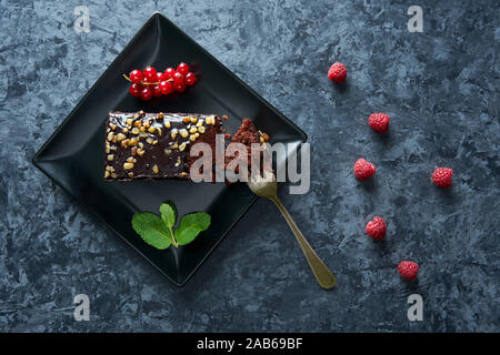 Brownie dessert torta con decorazioni in legno di noce con verde menta, ribes rosso e i lamponi sulla piastra nera. Foto Stock