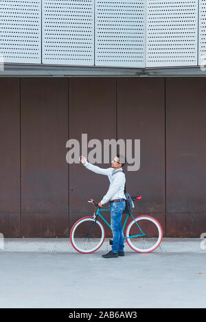 Hipster uomo prendendo un selfie . Egli è il pendolarismo, egli ha un ingranaggio fisso bike. Stile di vita, di viaggio e di concetti di sostenibilità. Foto Stock