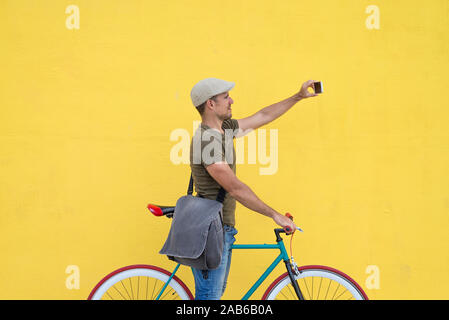Hipster uomo prendendo un selfie . Egli è il pendolarismo, egli ha un ingranaggio fisso bike. Stile di vita, di viaggio e di concetti di sostenibilità. Foto Stock