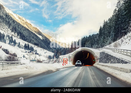 In inverno la strada alpina di paesaggio con tunnel, foresta, montagne e cielo blu su sfondo a bright freddo giorno di sole. Viaggio in auto famiglia viaggio Foto Stock