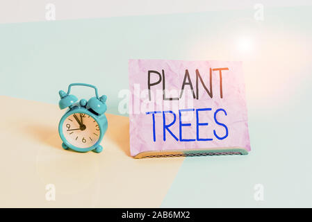 La grafia la scrittura di testo pianta alberi. Foto concettuale processo di piantare un albero per la successiva coltivazione dei terreni e la silvicoltura formato Mini sveglia accanto a un Pap Foto Stock