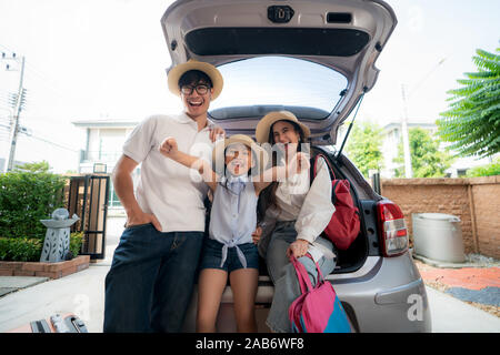 Ritratto di famiglia asiatica con padre, madre e figlia sembra felice mentre prepara la valigia in un auto per vacanza. Girato in casa garage. Foto Stock