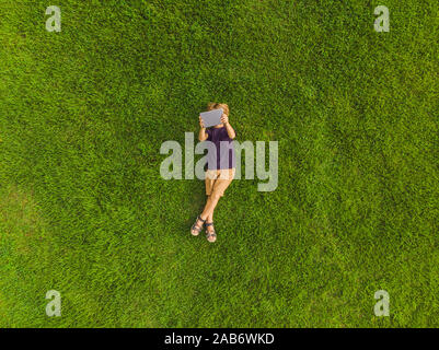 Ragazzo sdraiati sull'erba nel parco e guarda la compressa. Foto da fuco, quadracopter Foto Stock