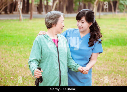 Infermiera sorridente aiutando senior donna passeggiare intorno al parco Foto Stock