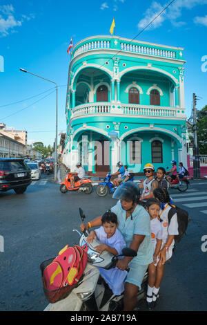 Un motociclista wth i suoi tre figli sulla sua moto passa davanti ad un stile Cino-portoghese casa nella zona vecchia della città nella città di Phuket, Tailandia Foto Stock