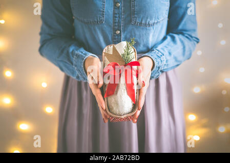 Close up della donna e delle sue mani tenendo in casa torta stollen avvolto come un dono di fronte le luci di Natale. Messa a fuoco selettiva. Foto Stock