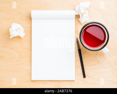 Aprire il notebook con un bianco per pulire foglio note e disegno, carta stropicciata, matita e la tazza di tè. Legno chiaro sfondo, vista dall'alto. Foto Stock