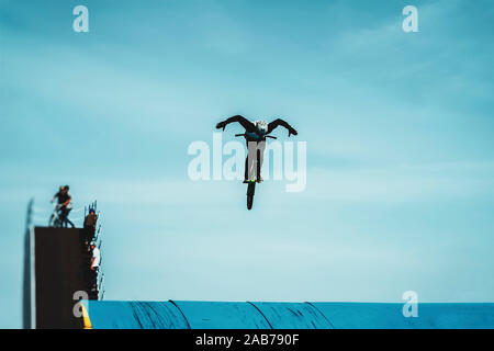 Silhouette di un irriconoscibile giovani bike rider antenna di eseguire trick BMX contro il cielo blu. Sport estremo, cultura giovanile Foto Stock