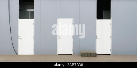 Tre nuovi white porte blindate in acciaio grigio parete di un ambiente urbano incompiuto centro commerciale Panorama Foto Stock