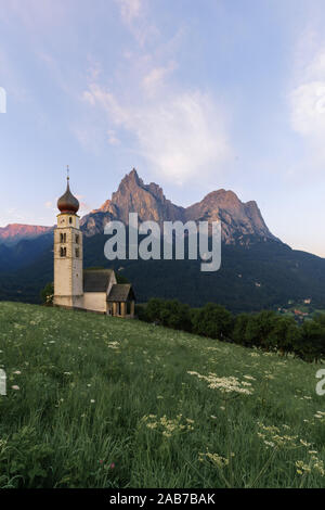 Sunrise paesaggi della chiesa di St. Valentin sulla collina erbosa con vista di aspre cime del monte Sciliar con alpenglow in background in valle o Foto Stock