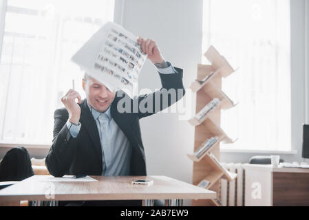 Un bel uomo seduto in ufficio e gettando papers in aria Foto Stock