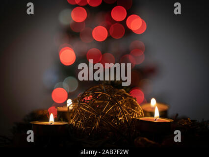 Avvento o ghirlanda di Natale con quattro candele accese. Chiudere l'immagine. Al di fuori della messa a fuoco albero di natale in background. Bokeh di luci di Natale. Foto Stock