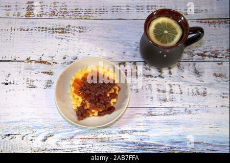 Una ceramica nera tazza di tè con una fettina di limone e una piastra di cialde Viennese con confettura di fragole. Vista da sopra. Foto Stock