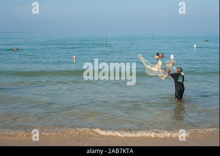 16.11.2019, Phuket, Thailandia, Asia - vacanzieri bagnarsi nel mare sulla spiaggia di Karon come un pescatore locale getta una rete da pesca. Foto Stock
